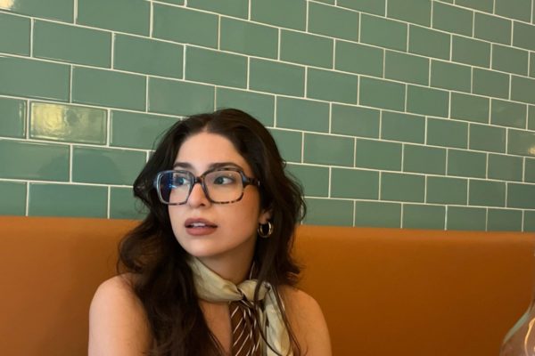 woman sitting at a booth wearing oversized glasses and a scarf tied around her neck